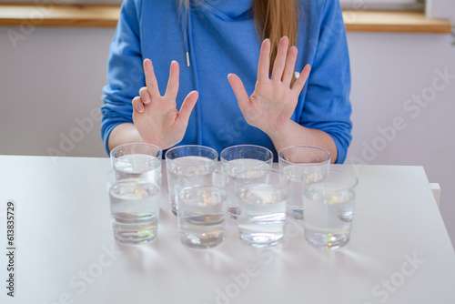 Osiem szklanek wody na stole i dziewczyna w niebieskiej bluzie