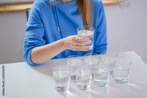 Kobieta pije wodę, przed nią stół na którym stoją napełnione szklanki