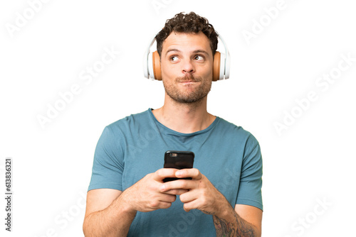 Brazilian man over isolated chroma key background listening music with a mobile and thinking © luismolinero