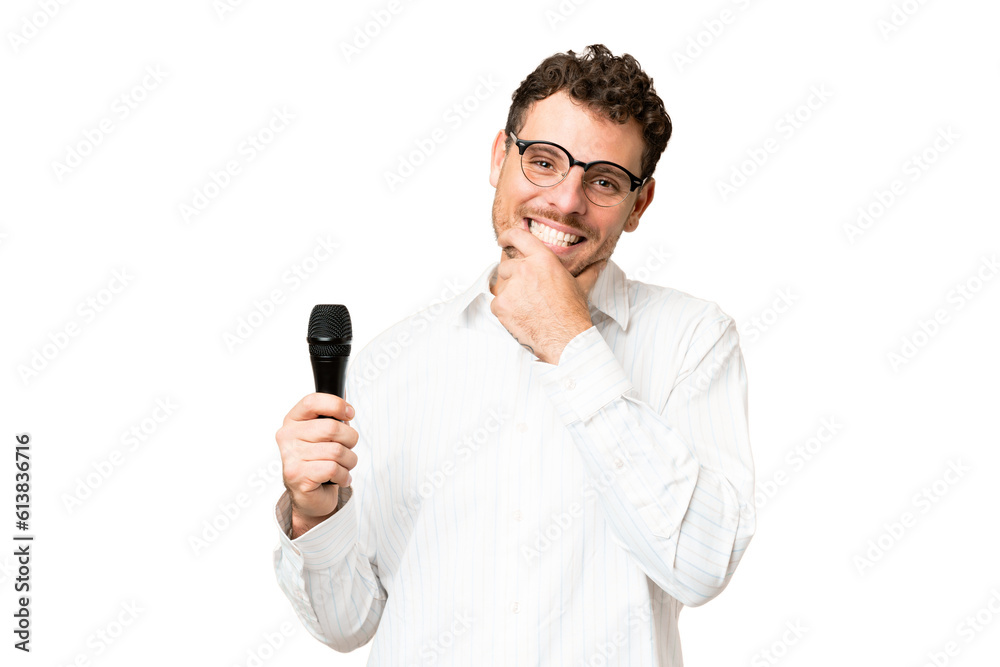 Brazilian man picking up a microphone over isolated chroma key background happy and smiling Brazilian man picking up a microphone over isolated chroma key background happy and smiling
