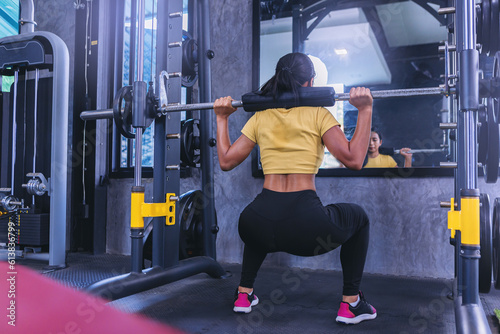 Fit young woman holding her hands with a weight barbell for pulling, squatting, workout in the fitness gym.