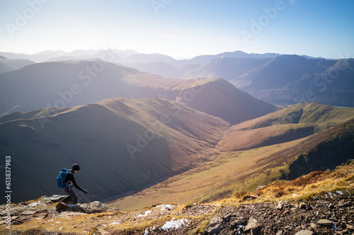 Obraz na płótnie A female hiker descending a rocky path towards Sail from Crag Hill with distant views of High Stile and Red Pike. w salonie