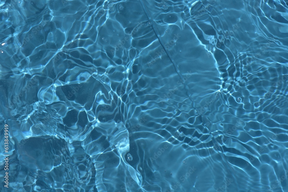 Obraz premium Blue water with ripples on the surface. Defocus blurred transparent blue colored clear calm water surface texture with splashes and bubbles. Water waves with shining pattern texture background.