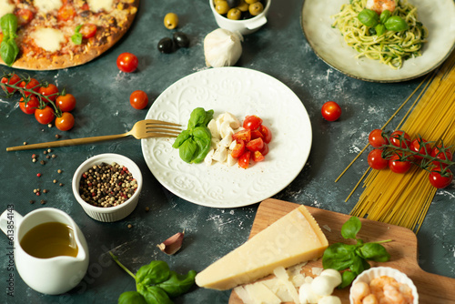 Full table of italian meals on plates Pizza, pasta, ravioli, carpaccio. caprese salad and tomato bruschetta on black background.
