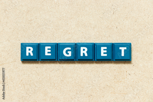 Tile alphabet letter in word regret on wood background