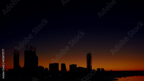 Sun rises over Perth City beginning with an orange glow developing into a bright sunny cloudless day. City buildings to north alongside Swan River to south.
