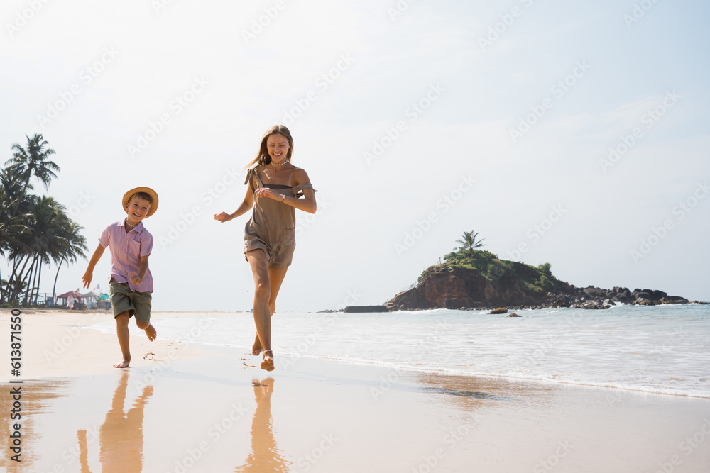 Beautiful young mother and son run at beach in sunny day and hugging