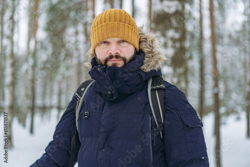 winter portrait of bearded caucasian man in knit hat and warm insulated jacket in snowy park