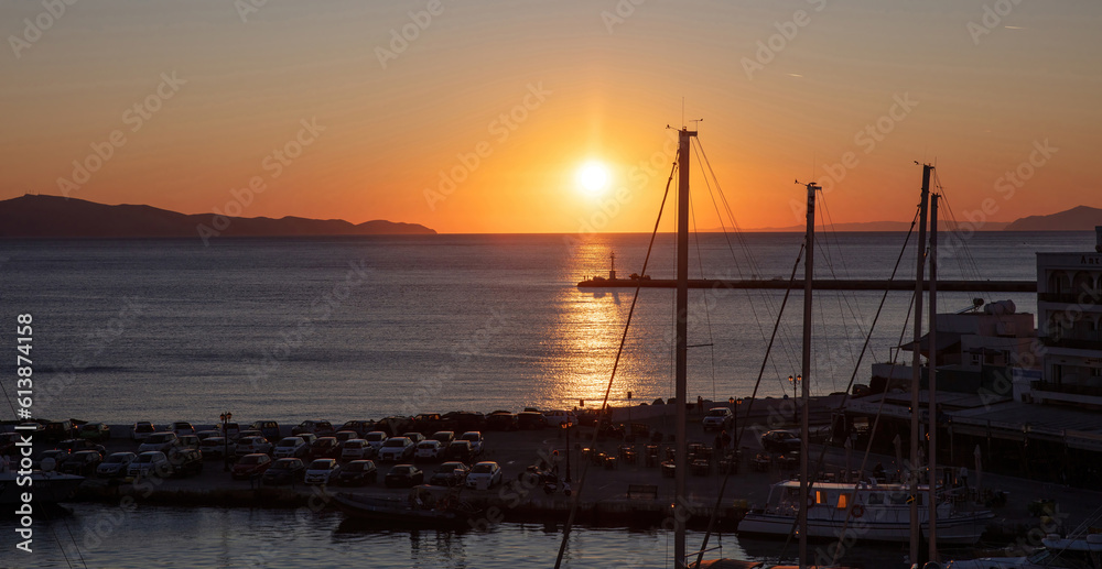 Sunset over Tinos island Cyclades Greece. Ship mast silhouette, port, golden sun colors sky and sea.