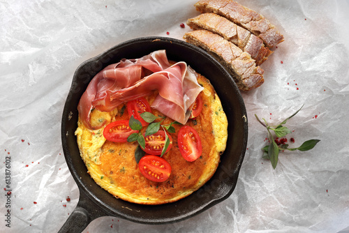 Omelette with tomato and prosciutto on a cast iron pan. Fresh vegetarian breakfast, top view, close-up.