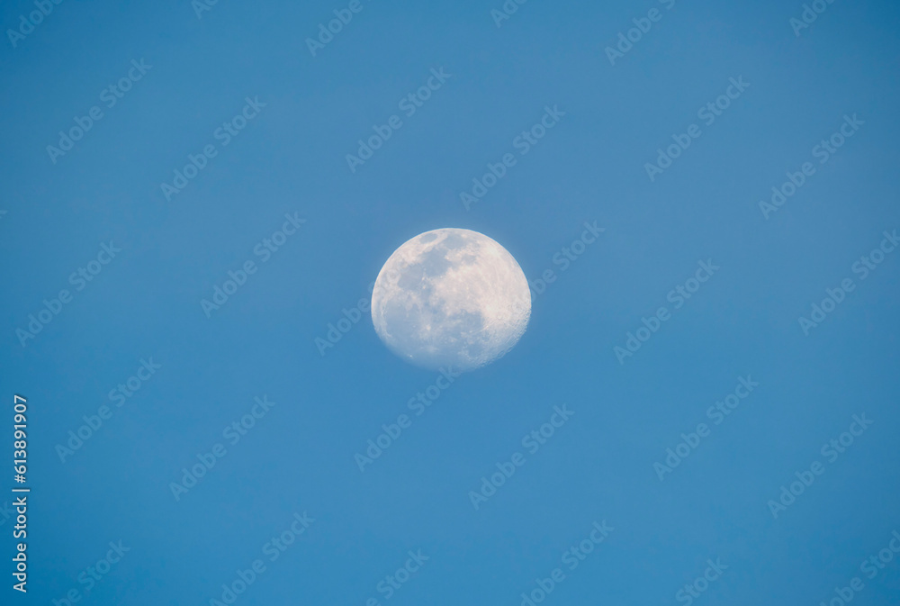 Bright full moon on blue sky during daylight. Round lunar disc