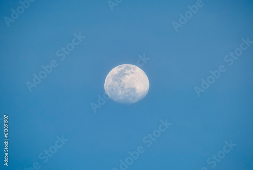 Bright full moon on blue sky during daylight. Round lunar disc