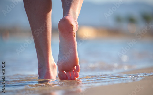 Close up of female feet walking barefoot on white grainy sand of golden beach on blue ocean water background © bilanol