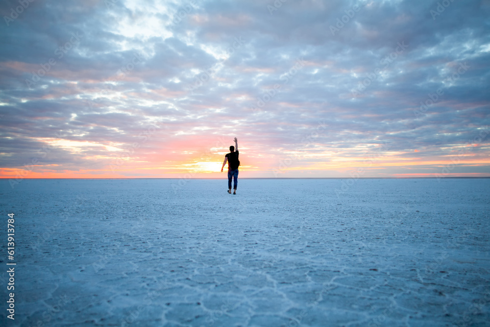 a man walking along the ocean and waving at the sunset