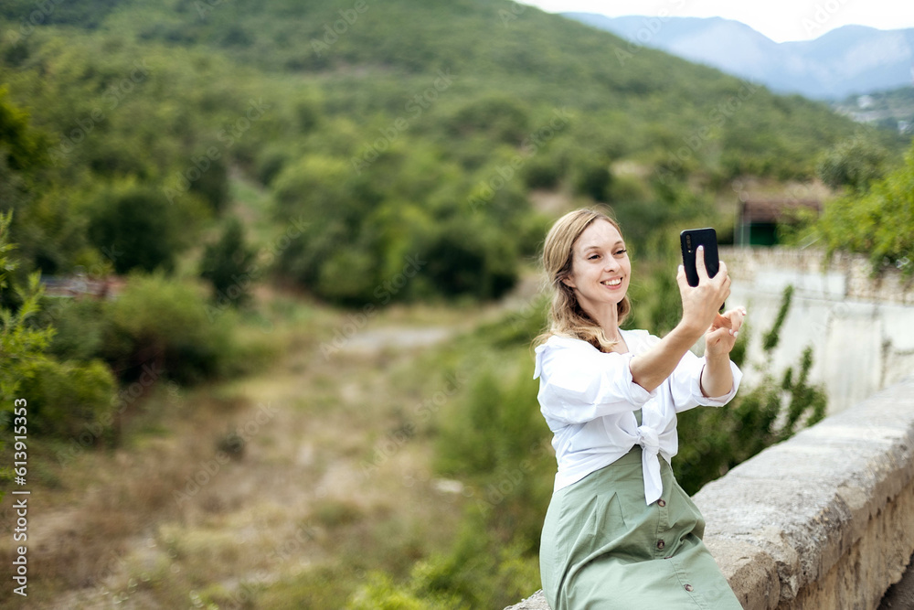 Naklejka premium Close-up portrait of a young woman who takes a selfie against the backdrop of beautiful nature, a concept of tourism, copy space