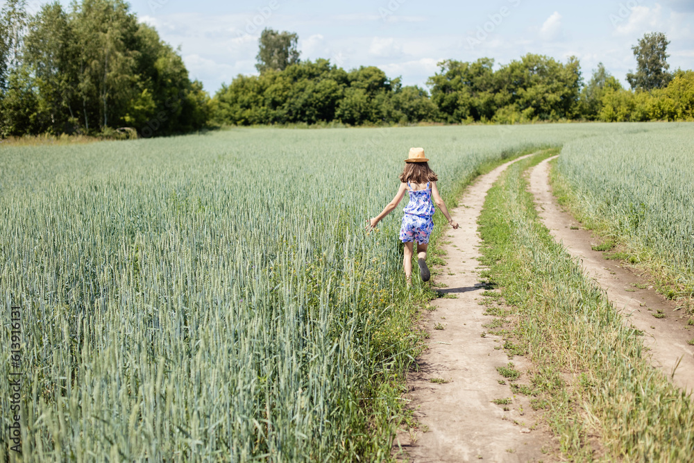Teenage girl running along a field with wheat, rear view, copy space Teenage girl running along a field with wheat, rear view, copy space