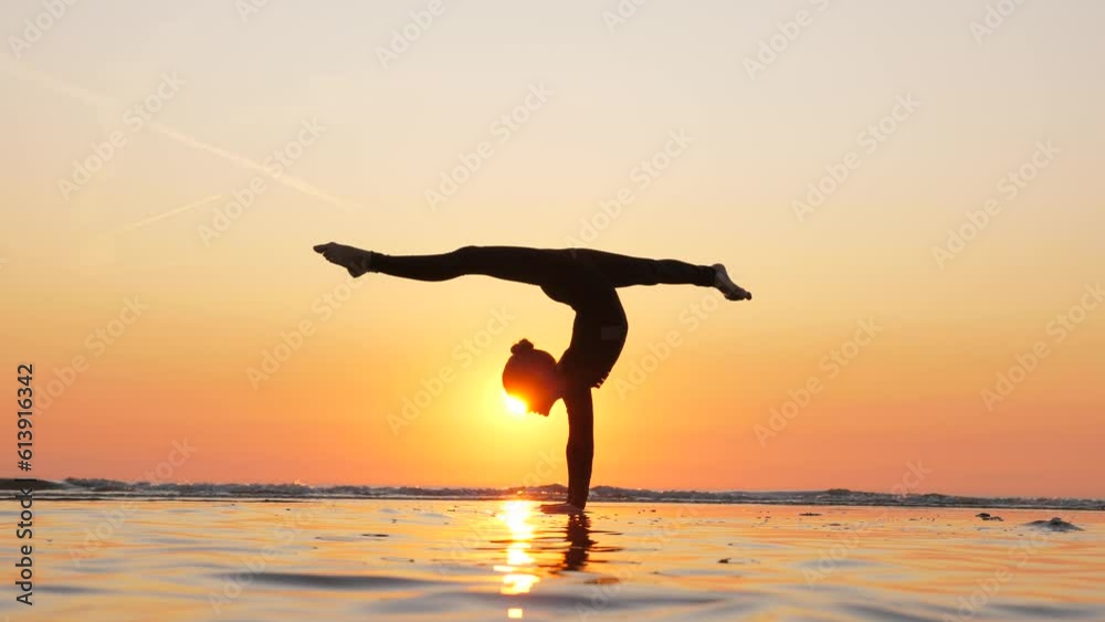 In picturesque setting of beautiful sunset beach, talented gymnast girl captivates with her impressive skills. With effortless grace, she performs handstand split, transitioning into single stag