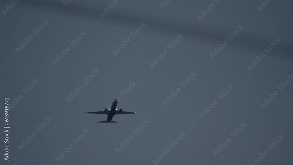 A passenger airplane with navigation lights on is ascending in the evening sky, captured through blurred power lines in the foreground A passenger airplane with navigation lights on is ascending in the evening sky, captured through blurred power lines in the foreground