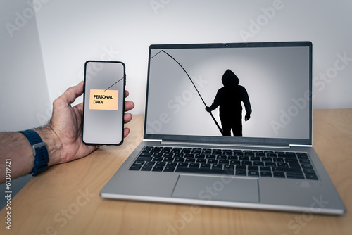 Silhouette of a hacker with a fishing rod on a laptop screen stealing personal data from a smartphone photo