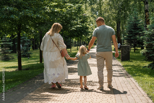Little cute girl in green summer dress with parents in city park on a walk summer family lifestyle Childhood happy family rear view