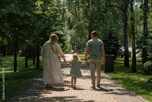 Little cute girl in green summer dress with parents in city park on a walk summer family lifestyle Childhood happy family rear view