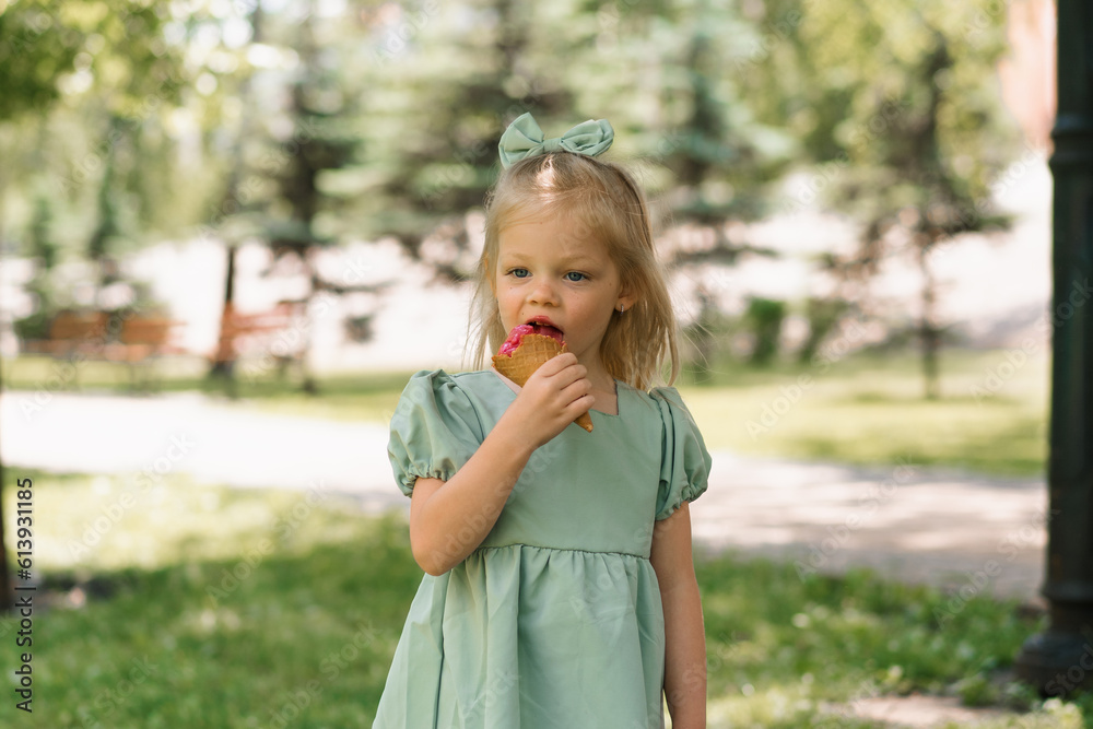 Fototapeta premium Little cute girl in green summer dress eating delicious ice cream Child with ice cream in city park summer family lifestyle Childhood