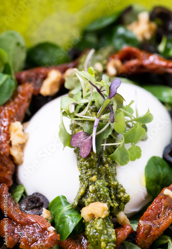 Vertical shot of a detail of colorful salad with burata cheese, pesto, pepper, black olives and canons