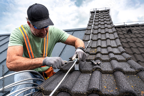 Work on the roof. An electrician installing a lightning rod conductor on a tiles roof.