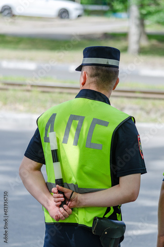 A traffic police officer is waiting for the offender. A view from the back, a bright vest and a striped rod.
