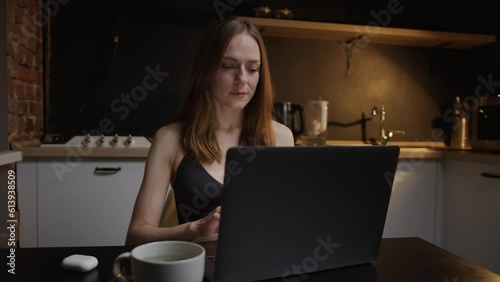 The concept of freelance work. A woman in front of a laptop in the kitchen at night