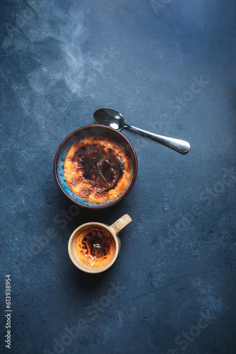 Fotografie Hot Crème brûlée in two cups, steaming and tasty with a spoon lying close, shot