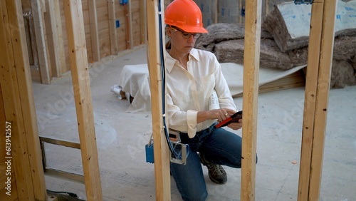 Happy woman mechanical engineer measuring electrical box in a new home construction using a touch tablet. photo