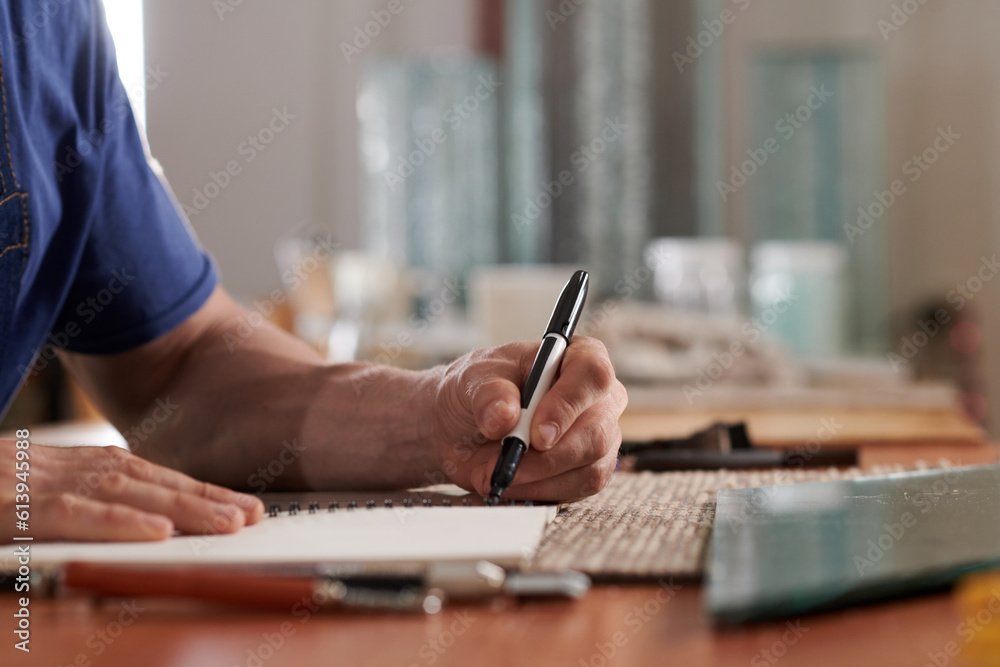 Close-up of man drawing sketches in notepad with pen while working in glass workshop Close-up of man drawing sketches in notepad with pen while working in glass workshop