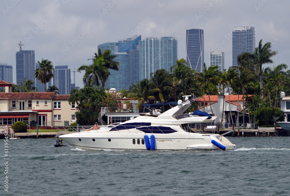 Obraz premium Party charter motor yacht leisurely cruising by luxury homes on Dilido Island,Miami Beach with downtown Miami tall building skyline in the background.
