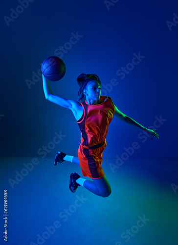 Slam dunk. Top view of young girl, basketball player throwing ball against blue studio background in neon light. Concept of professional sport, action and motion, game, competition, hobby, ad © master1305
