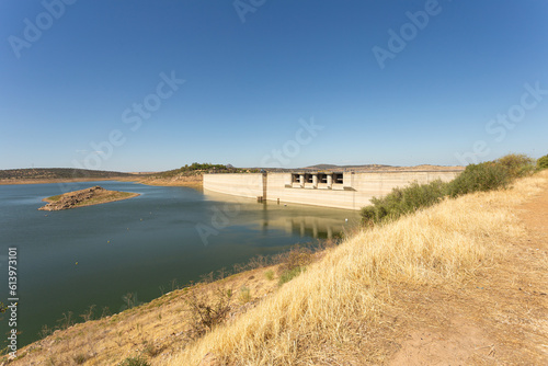 General view of the swamp dam in the area where it contains water. Hydroelectric power station. The water level is high despite the drought. There is a small mound in the middle of the water. Spain. 