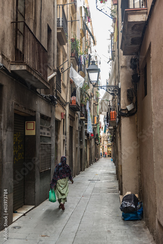 Headscarfed woman carrying a groceriesbag strawling through an Barcelona alleyway.