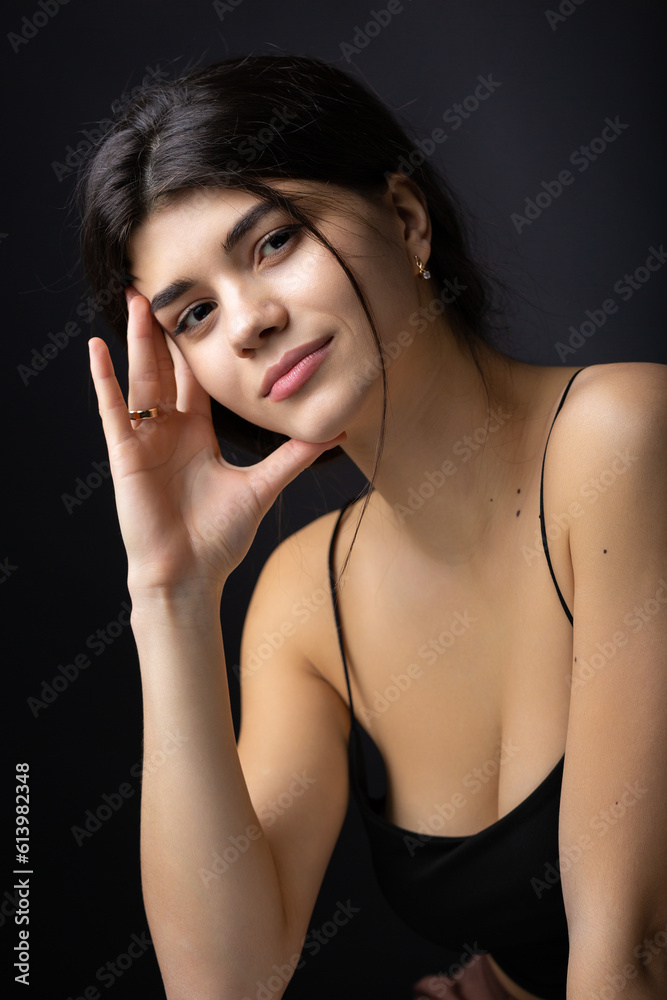 Classic studio portrait of a young brunette dressed in a black top, who is sitting on a chair against a black background. Classic studio portrait of a young brunette dressed in a black top, who is sitting on a chair against a black background.