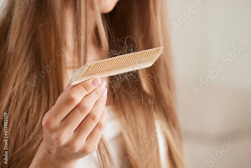The concept of the problem of hair loss. Shocked Asian woman looks at a lot of hair lost in her hand and comb.