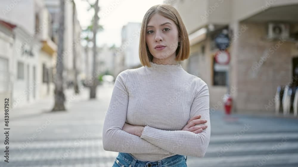 Young blonde woman standing with serious expression and arms crossed ...