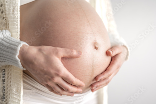Pregnant woman gently holding her naked round belly in final month of pregnancy. Third trimester - week 36. Close up. Side view. White background. Bright shot.