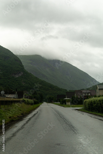 Wet road in the small town in big Norway valley located between the mountains during cloudy day