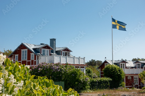 Traditional Swedish red house with white trims in residential area with flag of Sweden flying in summer picturesque scene photo