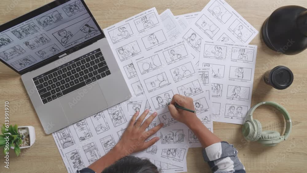Close Up Top View Of Asian Male Artist Looking At Sketching Concept On A Laptop And Drawing Storyboard On Table With Headphones In The Studio
