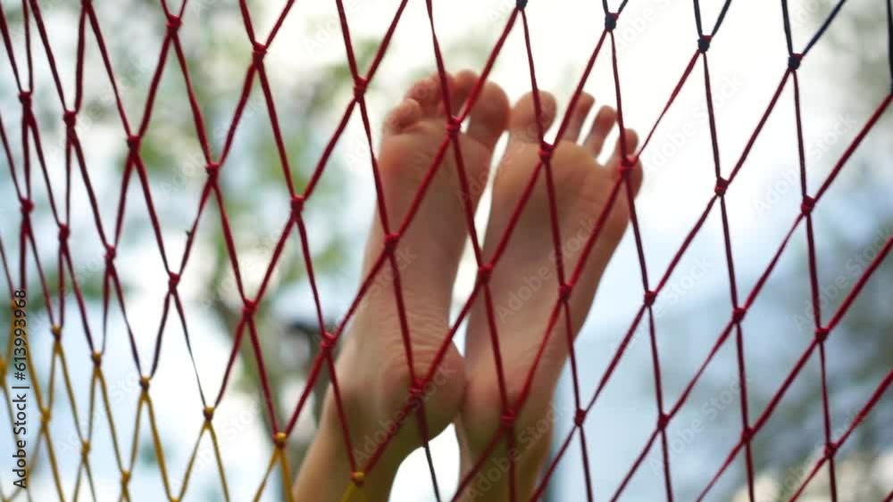 Pair of bare long child feet with long toes resting in hammock net during summer