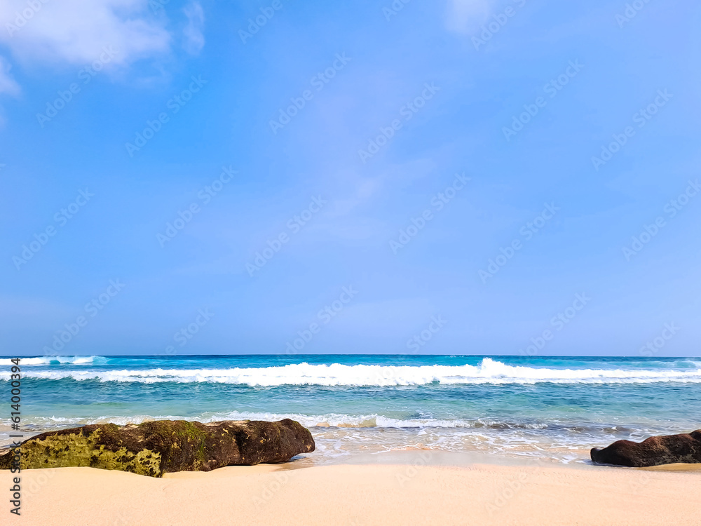 View of beautiful beach with white sand, rocks and calm waves under clear blue sky. Summer vacation concept. Ngudel Beach, Malang, Indonesia View of beautiful beach with white sand, rocks and calm waves under clear blue sky. Summer vacation concept. Ngudel Beach, Malang, Indonesia