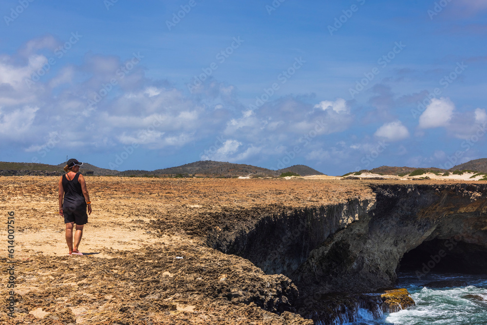 Beautiful view of rocky coast of Caribbean sea and woman standing on shore and looking into distance. Aruba island.