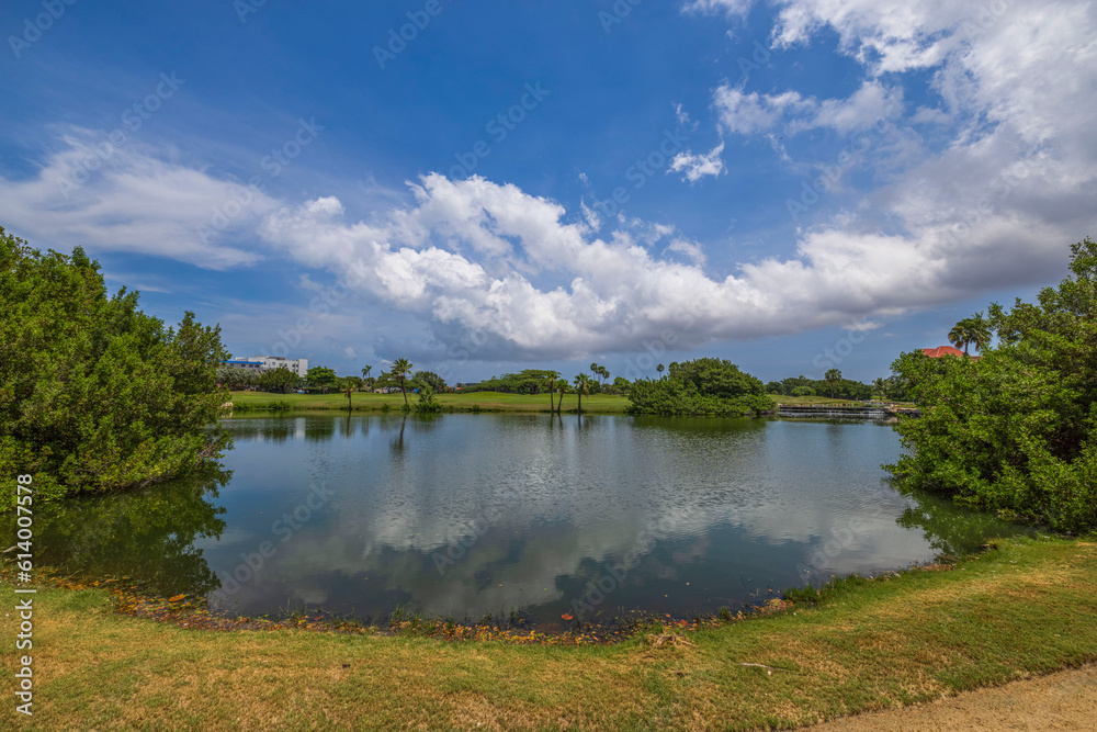 Beautiful view of lake and green golf courses on island of Aruba on blue sky with white clouds background.