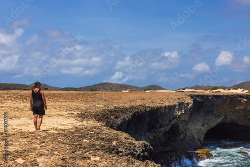 Beautiful view of rocky coast of Caribbean sea and woman standing on shore and looking into distance. Aruba island. © Alex