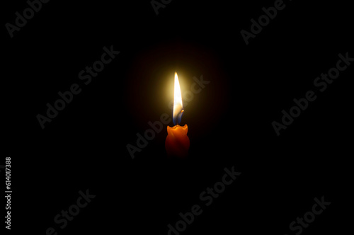 A single burning candle flame or light glowing spiral orange candle on black or dark background on table in church for Christmas, funeral or memorial service with copy space
